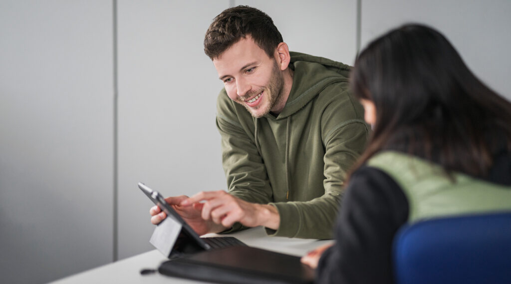 Mitarbeiter der Stadtwerke erklärt einer Kundin etwas auf einem Tablet und lächelt.