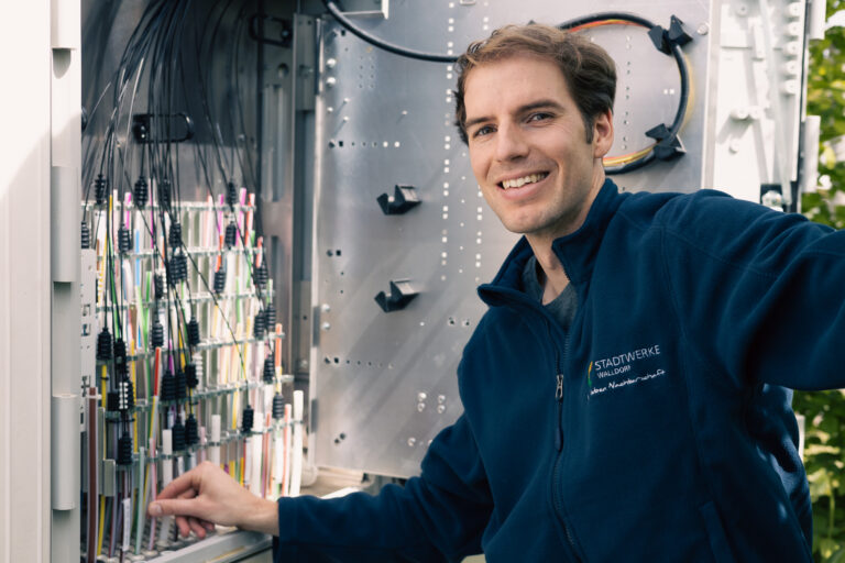 Mitarbeiter der Stadtwerke vor einem offenen Glasfaserschrank